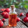 A bottle of rosehip seed oil with fresh rosehips on a table