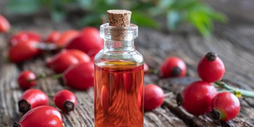 A bottle of rosehip seed oil with fresh rosehips on a table